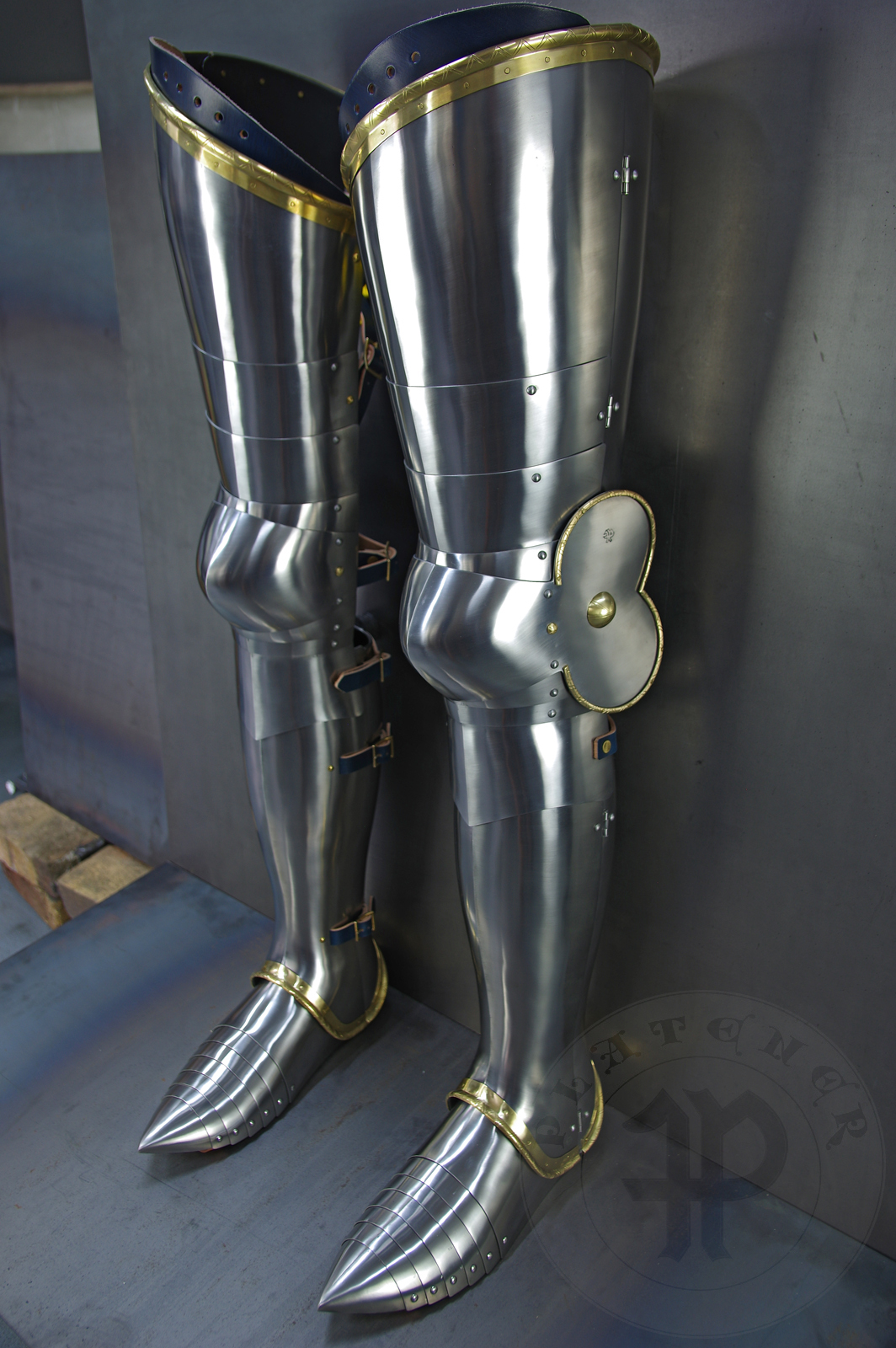 Late 14th/early 15th c. style full plate leg harness with brass decorations with a geometrical, hand filed pattern. Material: medium carbon and spring steel of various thickness: 1 mm; 1,2 mm and 1,5 mm; brass; vegetable tanned leather. Heat treatment: cuisses (thigh plates, lames, poleyns and demi-graves) heat hardened and tempered up to 42 HRC.